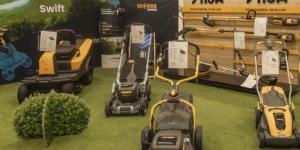 verschiedene Produkte der Marke STIGA im Schauraum präsentiert. Aufsteller mit Motorsense, Heckenschere usw. Davor auf künstlichem Teppich Rasenmäher.
